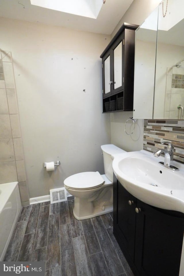 full bathroom with backsplash, a skylight, toilet, and hardwood / wood-style flooring