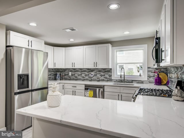 kitchen featuring white cabinets, stainless steel appliances, sink, kitchen peninsula, and light stone counters