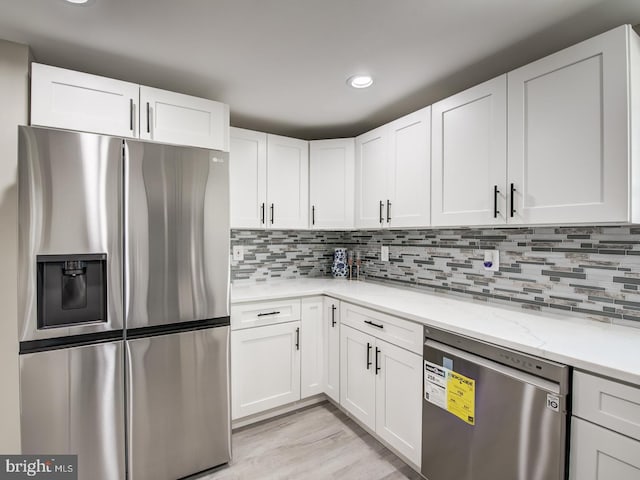 kitchen featuring appliances with stainless steel finishes, white cabinetry, tasteful backsplash, light stone counters, and light hardwood / wood-style flooring