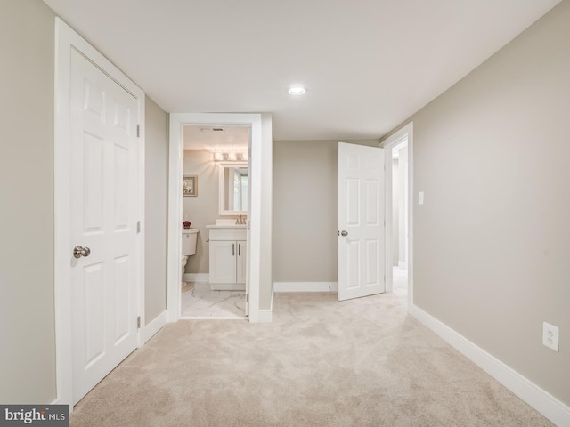 unfurnished bedroom with light colored carpet, ensuite bathroom, and sink