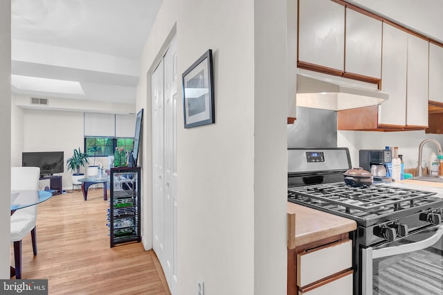 kitchen with sink, white cabinetry, light hardwood / wood-style flooring, and stainless steel gas range