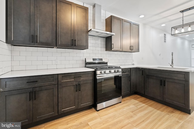 kitchen featuring pendant lighting, stainless steel range with gas cooktop, sink, wall chimney exhaust hood, and light wood-type flooring