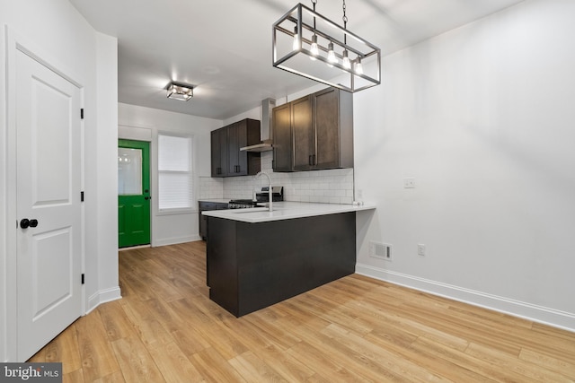 kitchen with sink, wall chimney range hood, light hardwood / wood-style floors, a kitchen bar, and dark brown cabinets