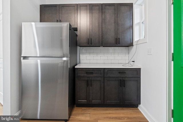 kitchen featuring dark brown cabinets, stainless steel fridge, light hardwood / wood-style floors, and tasteful backsplash