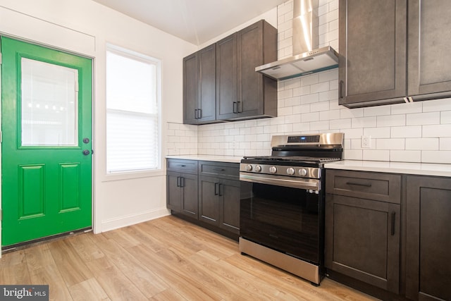 kitchen featuring backsplash, stainless steel range, dark brown cabinets, wall chimney range hood, and light hardwood / wood-style floors