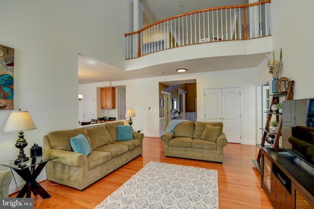 living room with baseboards, light wood-type flooring, and a towering ceiling