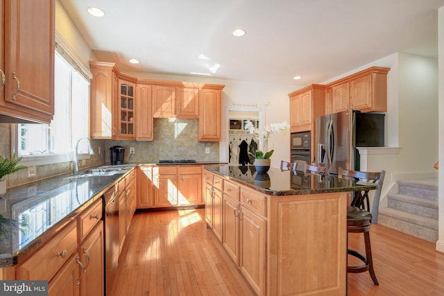 kitchen with dark stone countertops, a kitchen island, a breakfast bar, black appliances, and light wood-type flooring