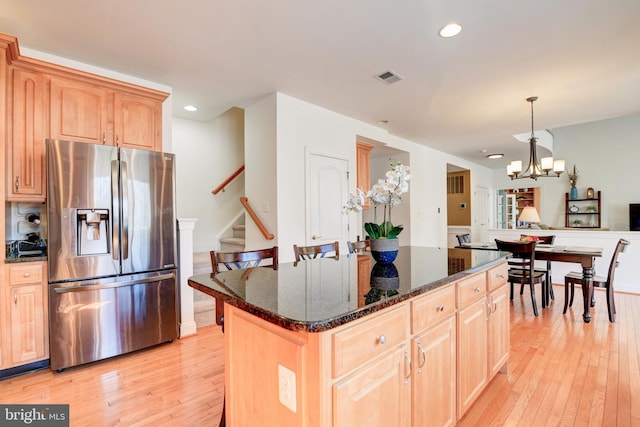 kitchen featuring dark stone counters, stainless steel fridge, light wood-style flooring, and light brown cabinets