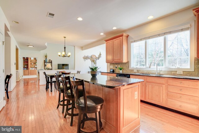 kitchen featuring visible vents, light wood-type flooring, light brown cabinets, a sink, and a kitchen breakfast bar