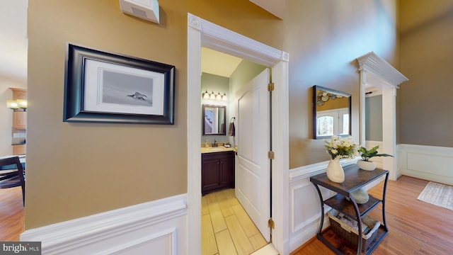 corridor with a wainscoted wall, a decorative wall, light wood-style floors, and a sink