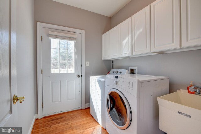 laundry area with cabinet space, washing machine and dryer, light wood finished floors, and a sink