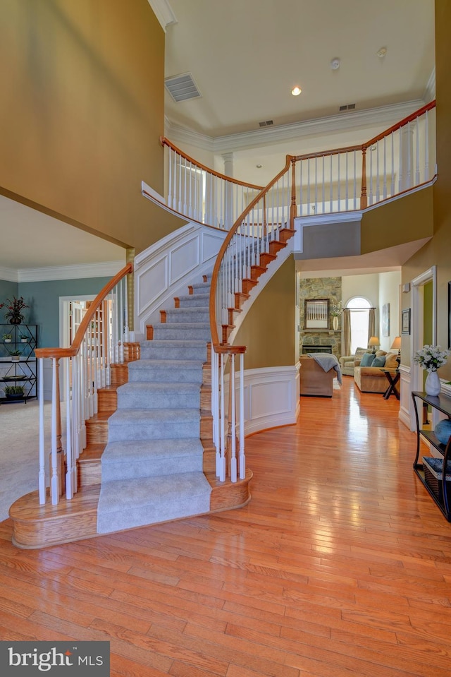 stairway with visible vents, ornamental molding, hardwood / wood-style flooring, a decorative wall, and a towering ceiling