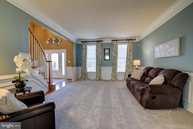 carpeted living area with a decorative wall, wainscoting, stairs, and ornamental molding