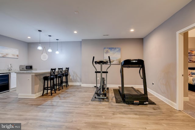 workout area featuring wet bar, light wood-style flooring, recessed lighting, and baseboards