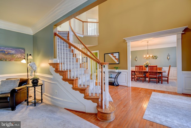 staircase with hardwood / wood-style floors, crown molding, an inviting chandelier, and wainscoting