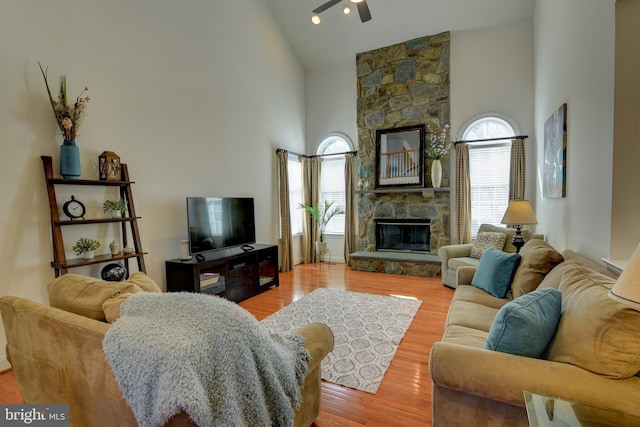 living area featuring plenty of natural light, high vaulted ceiling, a stone fireplace, and wood finished floors