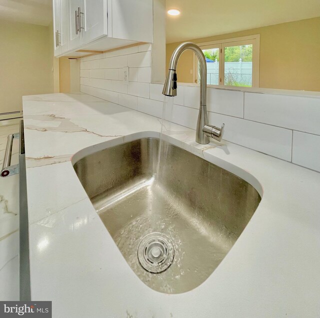 details featuring white cabinets, backsplash, light stone countertops, and sink