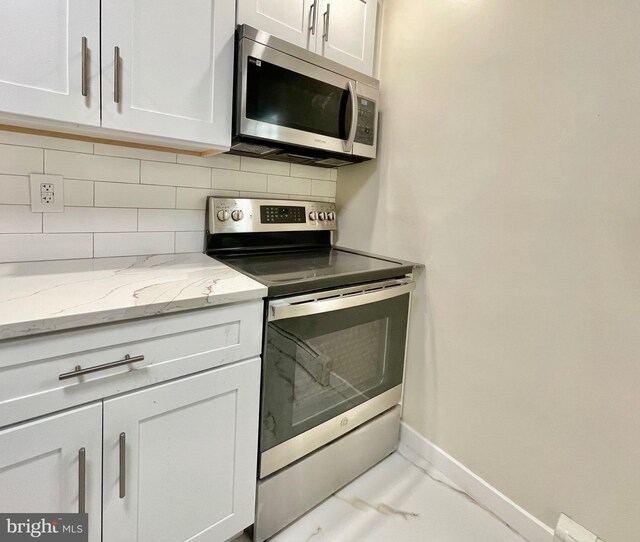 kitchen with white cabinets, appliances with stainless steel finishes, decorative backsplash, and light stone counters