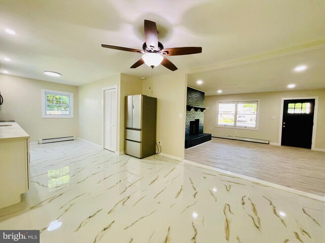 unfurnished living room with a brick fireplace, ceiling fan, and a baseboard heating unit