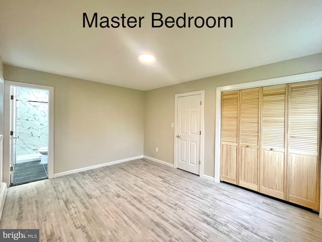 unfurnished bedroom featuring ensuite bathroom, a closet, and light hardwood / wood-style flooring