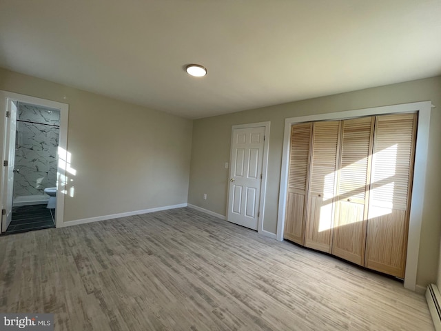 unfurnished bedroom featuring light wood-type flooring, ensuite bath, a closet, and a baseboard heating unit