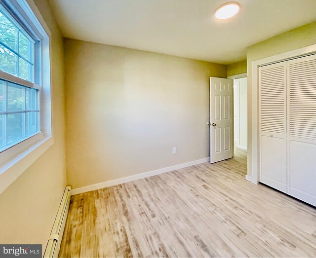 unfurnished bedroom with a closet, light hardwood / wood-style flooring, and baseboard heating