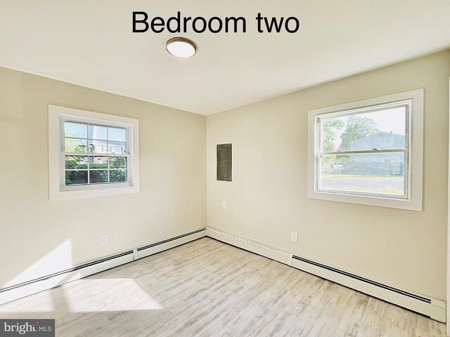 unfurnished room featuring light wood-type flooring, electric panel, a baseboard radiator, and plenty of natural light