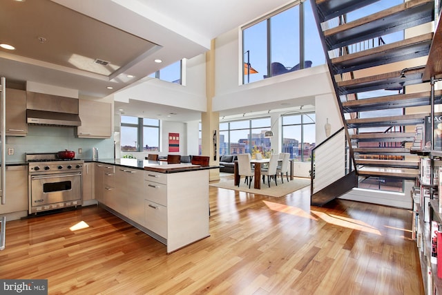 kitchen with light hardwood / wood-style floors, luxury stove, kitchen peninsula, exhaust hood, and a towering ceiling