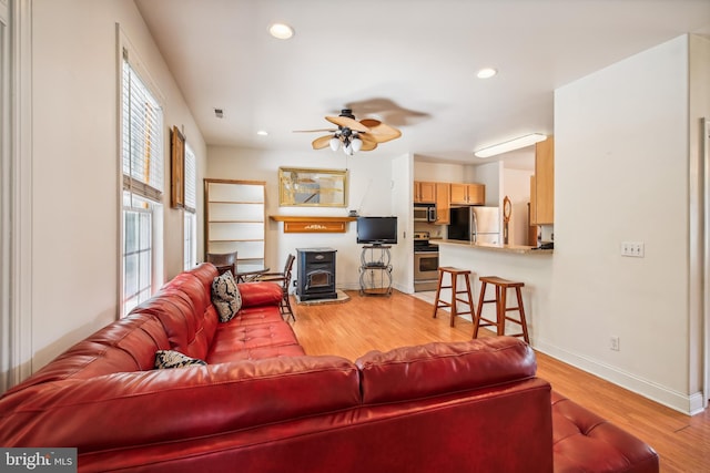 living room with a wood stove, light hardwood / wood-style flooring, and ceiling fan