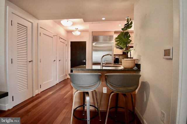 kitchen with a breakfast bar, kitchen peninsula, wood-type flooring, sink, and stainless steel built in refrigerator