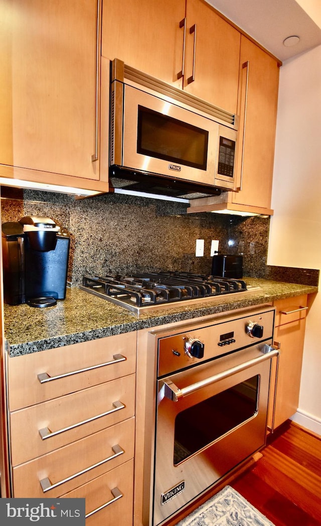 kitchen featuring decorative backsplash, appliances with stainless steel finishes, dark stone countertops, and dark hardwood / wood-style floors