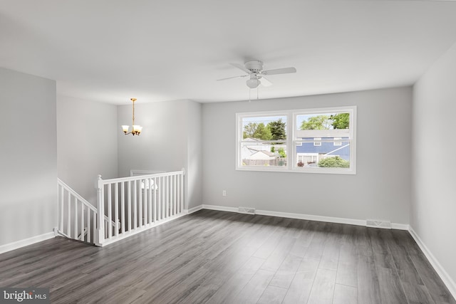 spare room with ceiling fan with notable chandelier and dark wood-type flooring