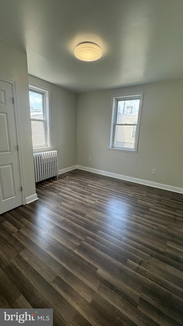 empty room featuring a wealth of natural light, dark hardwood / wood-style floors, and radiator