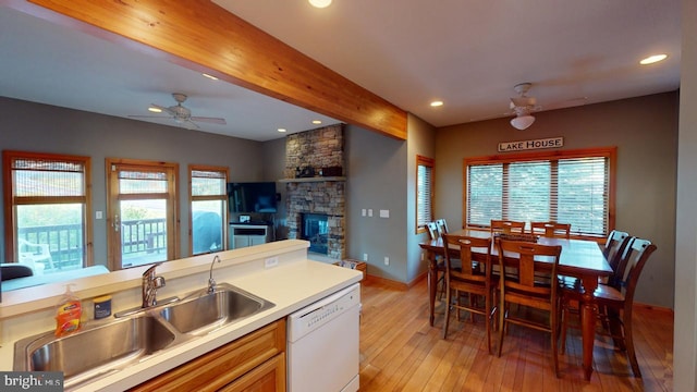 kitchen with dishwasher, light hardwood / wood-style floors, a stone fireplace, and plenty of natural light