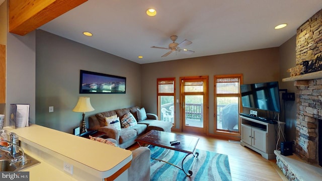 living room with ceiling fan, light hardwood / wood-style floors, beam ceiling, and a fireplace