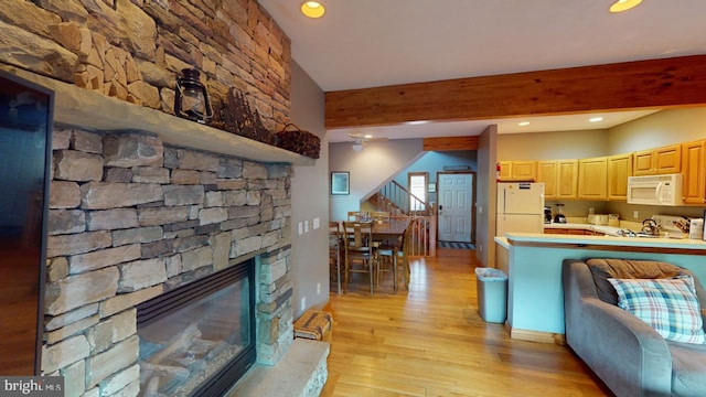 kitchen with beam ceiling, light brown cabinets, light hardwood / wood-style floors, white appliances, and a fireplace