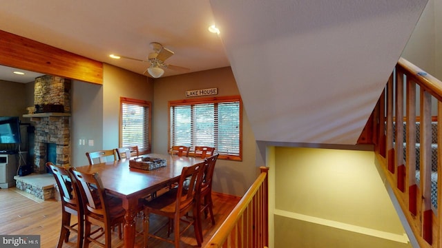 dining space with light hardwood / wood-style flooring, ceiling fan, and a stone fireplace