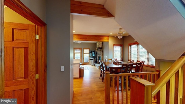 interior space with beam ceiling, hardwood / wood-style flooring, a stone fireplace, and ceiling fan