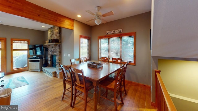 dining room featuring light hardwood / wood-style floors, a stone fireplace, plenty of natural light, and ceiling fan