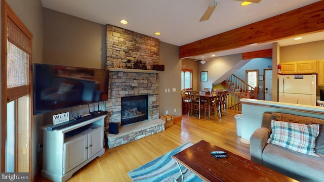 living room featuring a fireplace, ceiling fan, light hardwood / wood-style flooring, and beamed ceiling