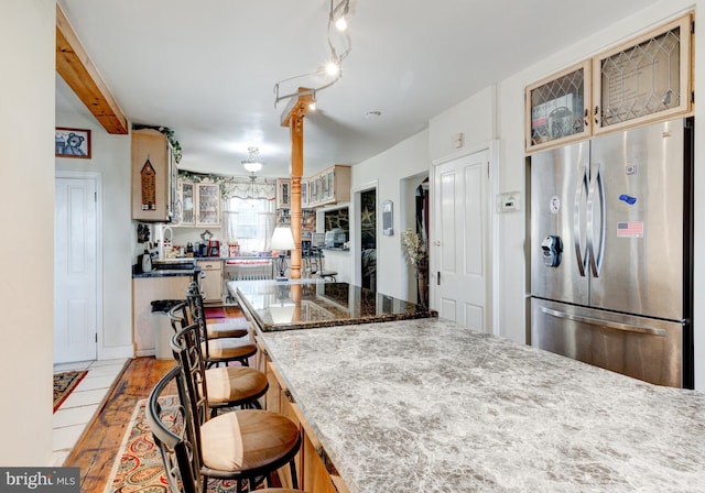 kitchen with a kitchen bar, stainless steel refrigerator, light stone countertops, and beamed ceiling