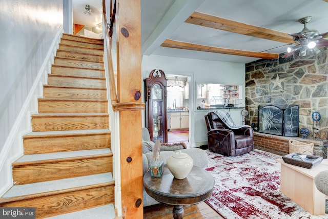 staircase with ceiling fan, a fireplace, beamed ceiling, and sink