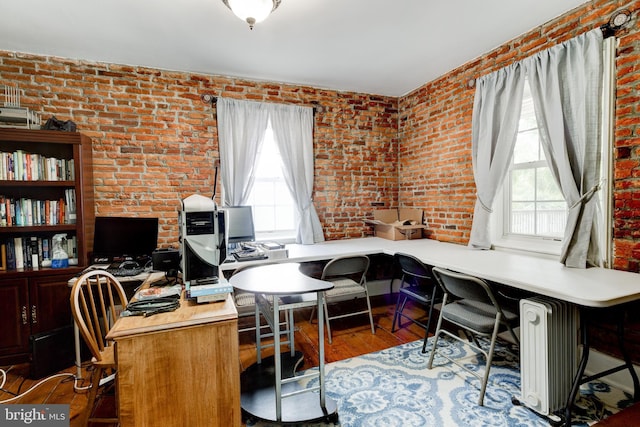 office space featuring radiator heating unit, light hardwood / wood-style floors, and brick wall