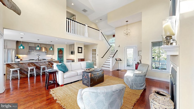 living room with a chandelier, a towering ceiling, dark wood-type flooring, and sink