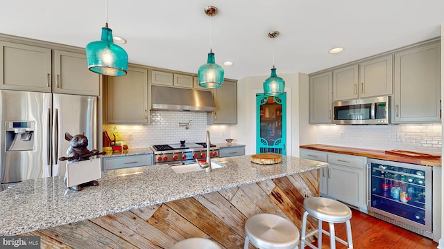 kitchen featuring dark wood-type flooring, exhaust hood, wine cooler, light stone counters, and stainless steel appliances