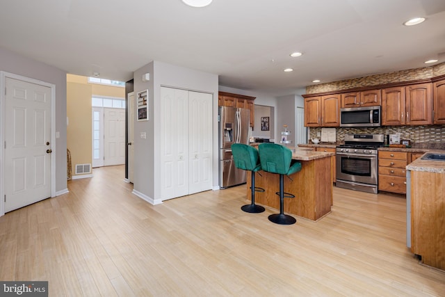 kitchen with light hardwood / wood-style floors, appliances with stainless steel finishes, tasteful backsplash, a kitchen island, and a breakfast bar area