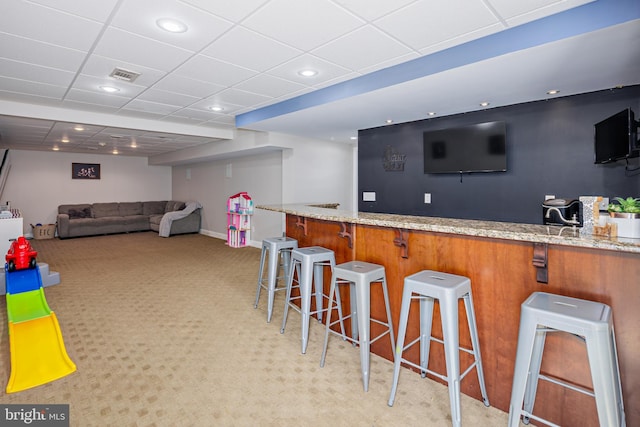 bar with a paneled ceiling, light colored carpet, and light stone countertops