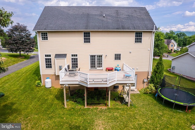 rear view of house with a lawn, a deck, and a trampoline