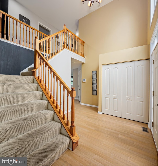 staircase with a towering ceiling, a notable chandelier, and hardwood / wood-style flooring