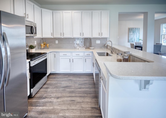 kitchen featuring kitchen peninsula, sink, dark hardwood / wood-style floors, appliances with stainless steel finishes, and white cabinetry